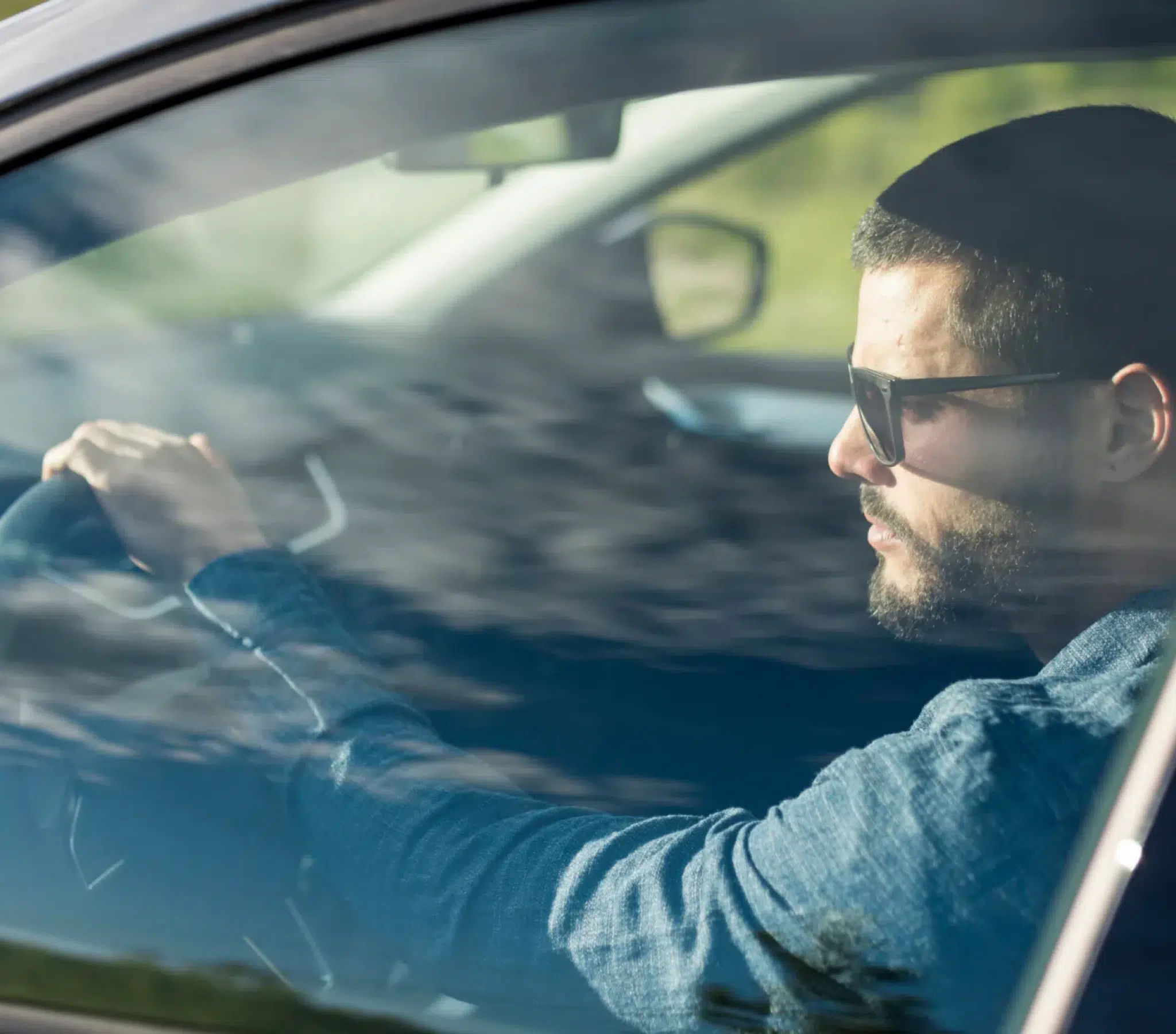 Man driving car, seen through tinted window.