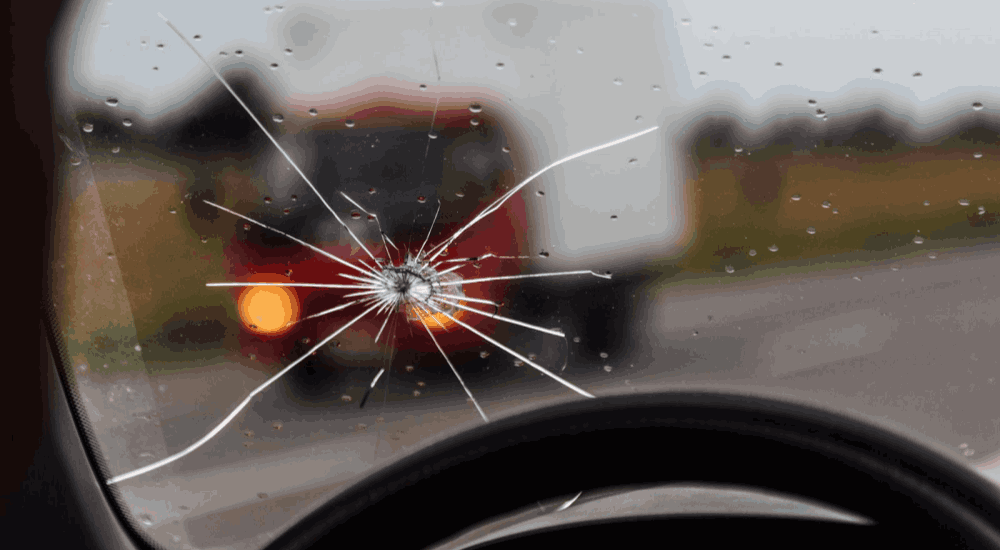 Close-up of a windshield with a crack and raindrops.